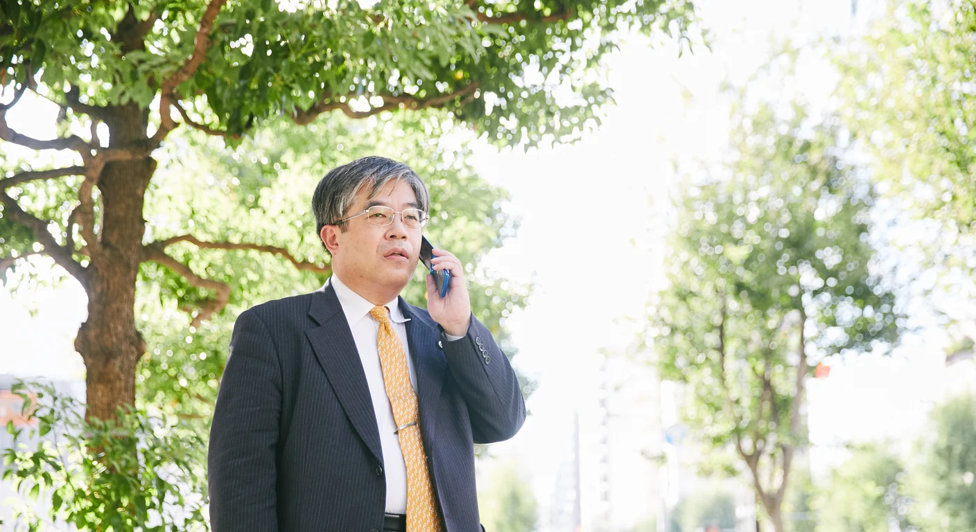 緑の並木道で電話をかける弁護士 依田敏泰